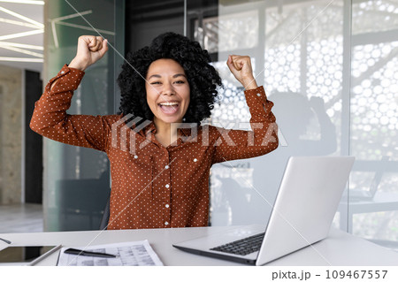 Happy female businesswoman joyfully raising her hands up in the office, African American woman got a promotion, won the lottery. 109467557