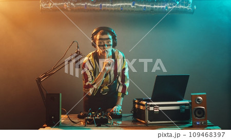 Cool disc jockey doing mute sign to haters, being focused on mixing techno music at nightclub performance. Woman artist with crazy makeup showing hush symbol to keep silence. Tripod shot. 109468397