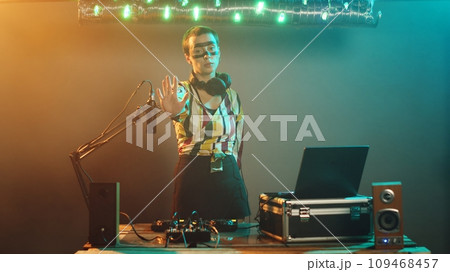 Crazy club musician raising palm to show denial and stop symbol on stage, mixing modern techno sounds on DJ turntables. Performer using audio stereo instruments, adjusting buttons. Tripod shot. Crazy club musician raising palm to show denial and stop symbol on stage, mixing modern techno sounds on DJ turntables. Performer using audio stereo instruments, adjusting buttons. Tripod shot. 109468457