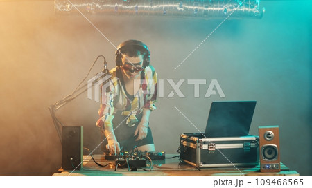 Female musician sticking tongue out and acting crazy, making silly faces and fooling around on nightclub stage. Confident cool disc jockey using turntables and microphone, mixing music. Female musician sticking tongue out and acting crazy, making silly faces and fooling around on nightclub stage. Confident cool disc jockey using turntables and microphone, mixing music. 109468565