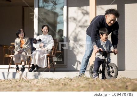 庭先で自転車の練習をする子どもを見守る父母 家族団欒の秋冬 庭先で自転車の練習をする子どもを見守る父母 家族団欒の秋冬 109470788