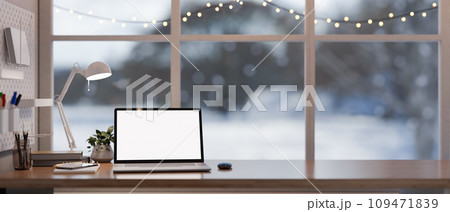 Home office workspace with a white-screen laptop on a wooden desk against the window on winter day. 109471839