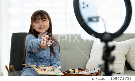 A cute young Asian girl is live streaming online to review the painting products while painting. A cute young Asian girl is live streaming online to review the painting products while painting. 109473752