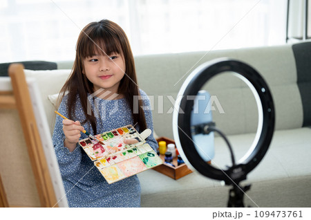 A pretty young Asian girl is live streaming on her social media while painting in the living room. 109473761