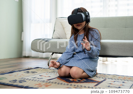 A cute young Asian girl is wearing VR headset and experiencing virtual reality game at home. A cute young Asian girl is wearing VR headset and experiencing virtual reality game at home. 109473770