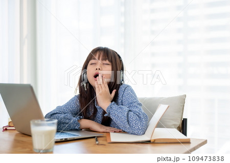 A cute young Asian girl is feeling tired and sleepy, yawning while studying online in her room. A cute young Asian girl is feeling tired and sleepy, yawning while studying online in her room. 109473838