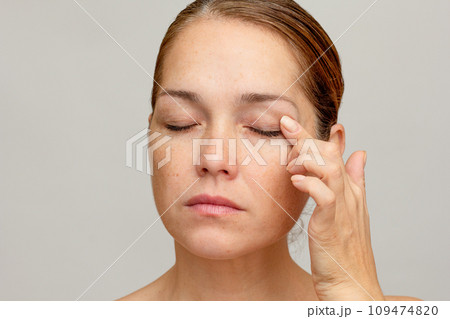 Middle aged caucasian woman of 40s with closed eyes holding finger on eyelid to show eyes aging Middle aged caucasian woman of 40s with closed eyes holding finger on eyelid to show eyes aging 109474820