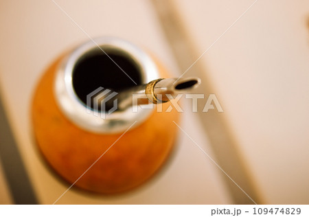 Mate calabash with bombilla on a light warm background. Healthy infused drink, classic Yerba mate tea on a table top view. Hot beverage on cafe terrace. Tableware. Traditional Latin America culture. Mate calabash with bombilla on a light warm background. Healthy infused drink, classic Yerba mate tea on a table top view. Hot beverage on cafe terrace. Tableware. Traditional Latin America culture. 109474829