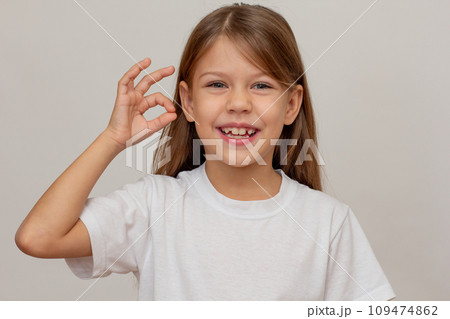 Portrait of caucasian happy little girl with open wide smile showing sign OK 109474862