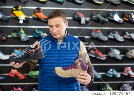 Man examine compare item of winter comfortable tracking shoes 109476464