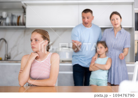 Upset teenage girl listening to disgruntled parents reprimanding her 109476790