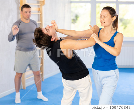 Self-defense class - a woman practices blows to the head of an attacking man under the guidance of trainer 109476845