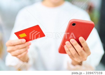 クレジットカードとスマートフォンを持つ女性の手元 109477339