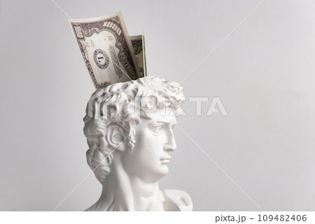 Antique male David statue's head with a wad of hundred-dollar cash banknotes isolated on a white background. 3d trendy cretive collage in magazine style. 3d contemporary art. Modern design Antique male David statue's head with a wad of hundred-dollar cash banknotes isolated on a white background. 3d trendy cretive collage in magazine style. 3d contemporary art. Modern design 109482406