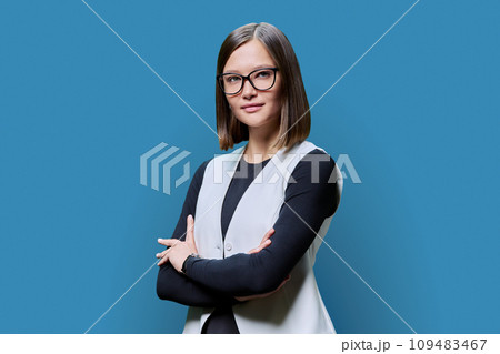 Young confident woman with crossed arms looking at camera on blue background Young confident woman with crossed arms looking at camera on blue background 109483467
