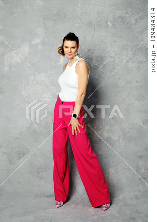 Joyful woman in pink wide trousers and white tank top posing on abstract grey background Joyful woman in pink wide trousers and white tank top posing on abstract grey background 109484314