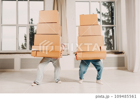 Happy young family couple man and woman moving carry heavy cardboard boxes in hands to new home apartment. Happy young family couple man and woman moving carry heavy cardboard boxes in hands to new home apartment. 109485561