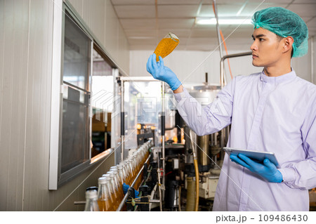 At the beverage bottling factory a quality control officer use tablet to ensure manufacturing line precision. machinery engineer inspects and maintains machines for proper basil or chia seed bottling. 109486430