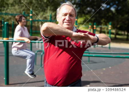 Elderly man and a woman are doing gymnastics on an open-air sports ground Elderly man and a woman are doing gymnastics on an open-air sports ground 109486524
