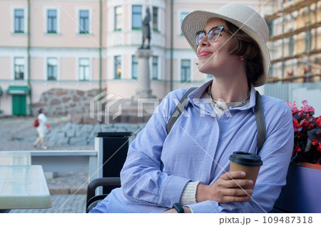 A girl drinks coffee from a paper cup in a coffee shop on the street of an ancient city A girl drinks coffee from a paper cup in a coffee shop on the street of an ancient city 109487318