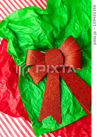 This is a photo of a red glitter bow on a green crumpled tissue paper with a red and white striped background. This is a photo of a red glitter bow on a green crumpled tissue paper with a red and white striped background. 109488366