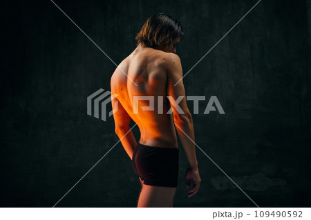 Healthy fit relief ack. Rear view of young shirtless man with muscular body standing in underwear against dark textured studio background Healthy fit relief ack. Rear view of young shirtless man with muscular body standing in underwear against dark textured studio background 109490592