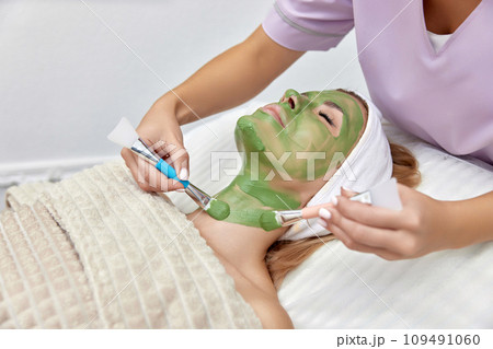 female beautician applies the mask to the face of beautiful woman in the spa salon. facial skin care 109491060