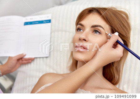 cosmetologist marking skin of caucasian woman with white pencil. facial marking for aesthetic procedure. cosmetologist marking skin of caucasian woman with white pencil. facial marking for aesthetic procedure. 109491099