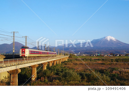 冠雪の大山を背景に日野川の長い鉄道橋梁を駆け抜ける標準ゆったりやくも色の381系特急やくも号 109491406
