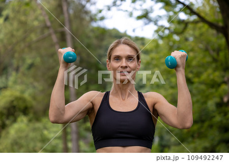Athletic woman training hands with dumbbells has workout in park. Athletic woman training hands with dumbbells has workout in park. 109492247