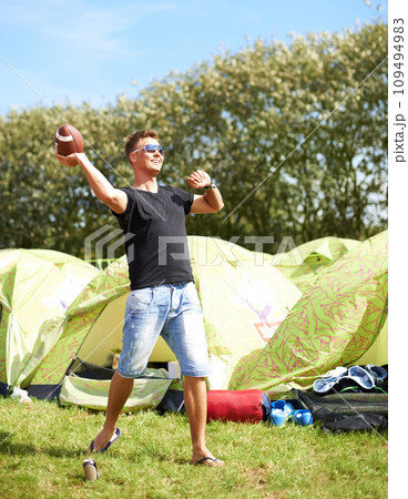 Man throw ball, camping and smile in nature outdoor at music festival, party carnival or celebration event in summer. Sports, play and person for rugby at tent, exercise game and happy to travel Man throw ball, camping and smile in nature outdoor at music festival, party carnival or celebration event in summer. Sports, play and person for rugby at tent, exercise game and happy to travel 109494983