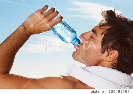 Young man, drinking water bottle or towel for workout with health body, fitness and vacation. Model, thirsty or natural glow with h2o drink for hydration or post cardio exercise by sky background 109495597