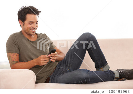 Man, phone or smile on sofa with relax, communication or conversation for break in living room of home. Person, face or happy with smartphone or technology on couch in lounge for text message or chat Man, phone or smile on sofa with relax, communication or conversation for break in living room of home. Person, face or happy with smartphone or technology on couch in lounge for text message or chat 109495968