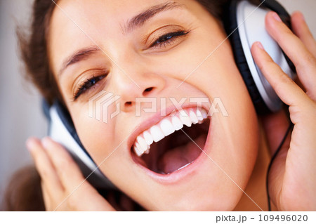 Excited, headphones and closeup of young woman listening to music, playlist or radio at home. Happy, technology and face of female person from Canada relax and streaming song or album in apartment. 109496020