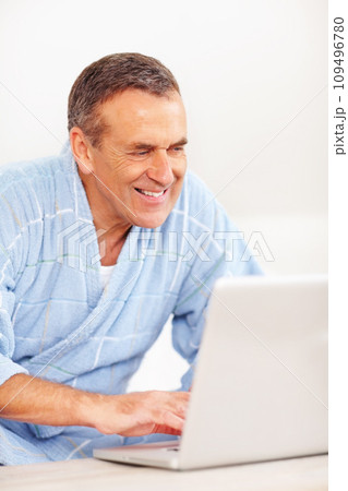 Bathrobe, morning and mature happy man on laptop for email, social media or streaming subscription on sofa. Internet search, couch and senior person on computer, website or networking in living room. 109496780