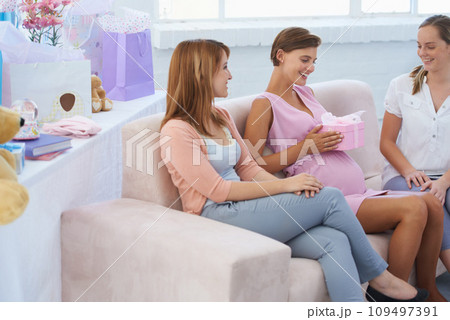 Happy women, baby shower and gift in living room couch, hand on belly. Pregnant lady, smile and excited for pregnancy, motherhood and celebrating child with friends in family home with present 109497391