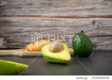 halved avocado on plate and croissant on a black background halved avocado on plate and croissant on a black background 109499049