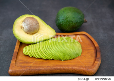 Top view of halved and finely sliced avocado on wooden plate on black background. 109499050