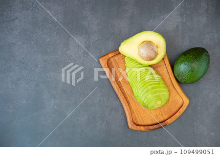 Top view of halved and finely sliced avocado on wooden plate on black background. 109499051