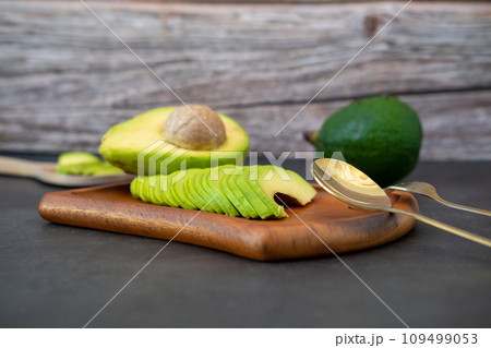halved and finely sliced avocado on wooden plate on black background. 109499053