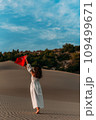 A beautiful dark-haired woman holds a Turkish flag in her hands, rear view. A woman is traveling in Turkey. A tourist on the background of Patara beach in Turkey. Vacation in Turkey. Turkish flag 109499671