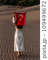 A beautiful dark-haired woman holds a Turkish flag in her hands, rear view. A woman is traveling in Turkey. A tourist on the background of Patara beach in Turkey. Vacation in Turkey. Turkish flag 109499672