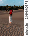 A beautiful dark-haired woman holds a Turkish flag in her hands, rear view. A woman is traveling in Turkey. A tourist on the background of Patara beach in Turkey. Vacation in Turkey. Turkish flag 109499673