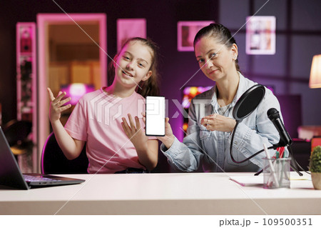 Media star daughter and mother excited to review newly launched mockup smartphone, comparing features with older models. Young internet show host filming video analyzing isolated screen smartphone 109500351