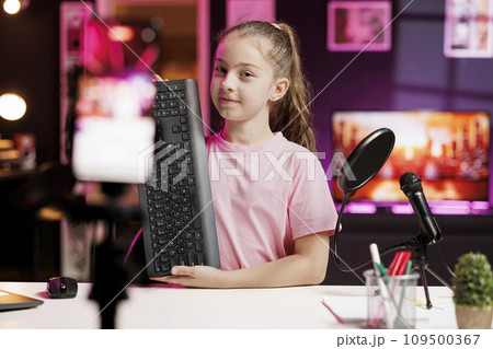 Smiling kid showing viewers mechanical keyboard received from sponsoring brand to promote it. Young online show host advertising wireless gaming computer peripheral from partnering company 109500367