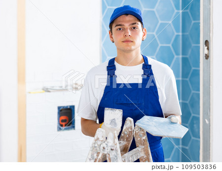 Construction worker in work clothes engaged in wall tiling work during overhauls indoors 109503836