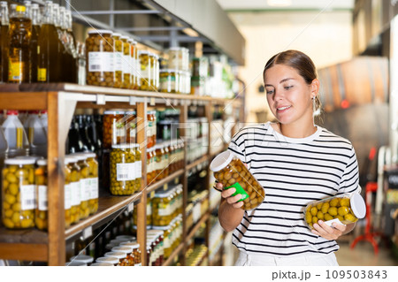 Young female shopper deciding between varieties of pickled olives in store 109503843