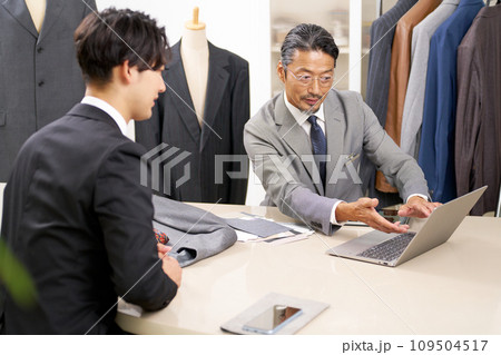 顧客にPCの画面を見せて商品説明をするスーツ販売スタッフ 109504517