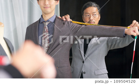 鏡の前で顧客の採寸をするテーラーのスタッフ 鏡の前で顧客の採寸をするテーラーのスタッフ 109504520