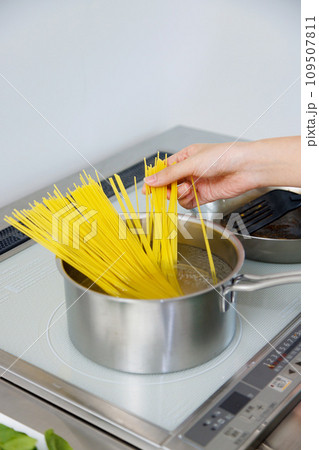 キッチンでスパゲッティを調理する女性 109507811